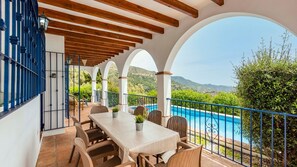A covered outdoor dining area with a pool view, featuring a table and chairs, and a railing overlooking a pool. - Villa Hugo Cómpeta by Ruralidays (Málaga)