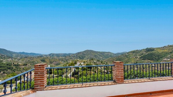 A balcony with a metal railing and brick pillars, overlooking a hilly landscape with scattered buildings. - Villa Hugo Cómpeta by Ruralidays (Málaga)