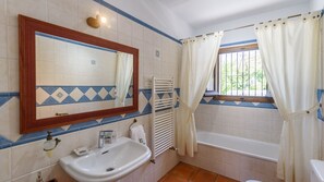 Bathroom with a sink, mirror, and bathtub, offering a view of the surrounding greenery.