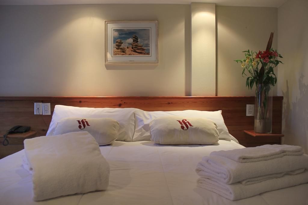 Una habitación de hotel con una cama bien hecha, un cuadro en la pared y un florero con flores en la mesita de noche.