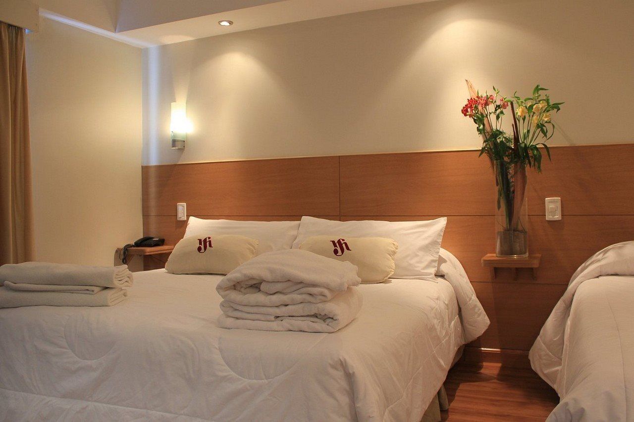 A hotel room with a large bed, two bedside tables, a nightstand, a vase with flowers, and a wall-mounted light.
