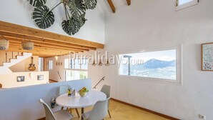 A modern living room with a dining area, a staircase, and a large window with a mountain view.