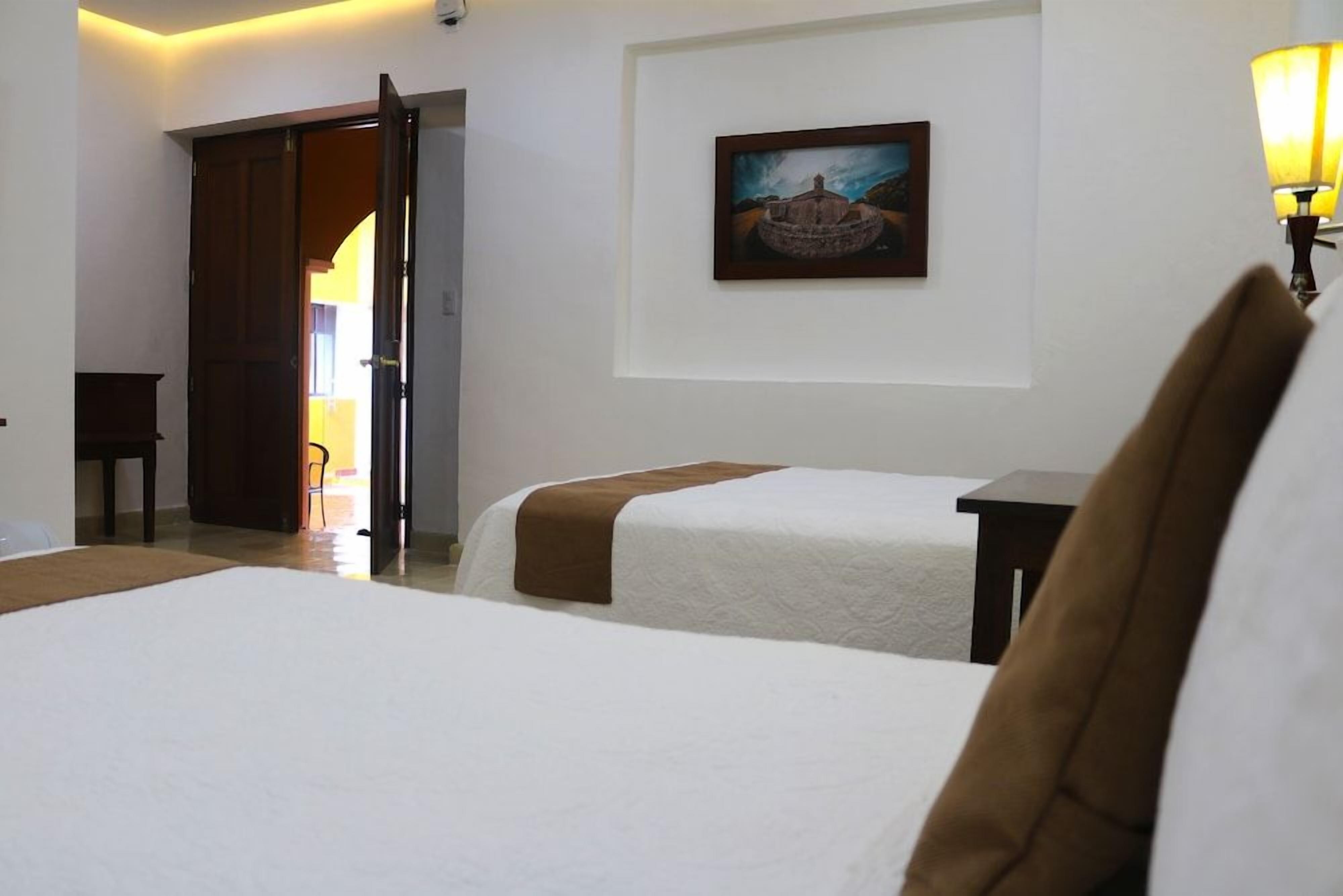 Una habitación de hotel con dos camas, un cuadro en la pared y una lámpara.
