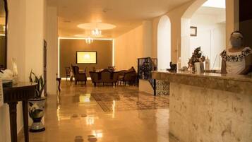 Un vestíbulo de hotel con mostrador de recepción, zona de estar y una pantalla grande.