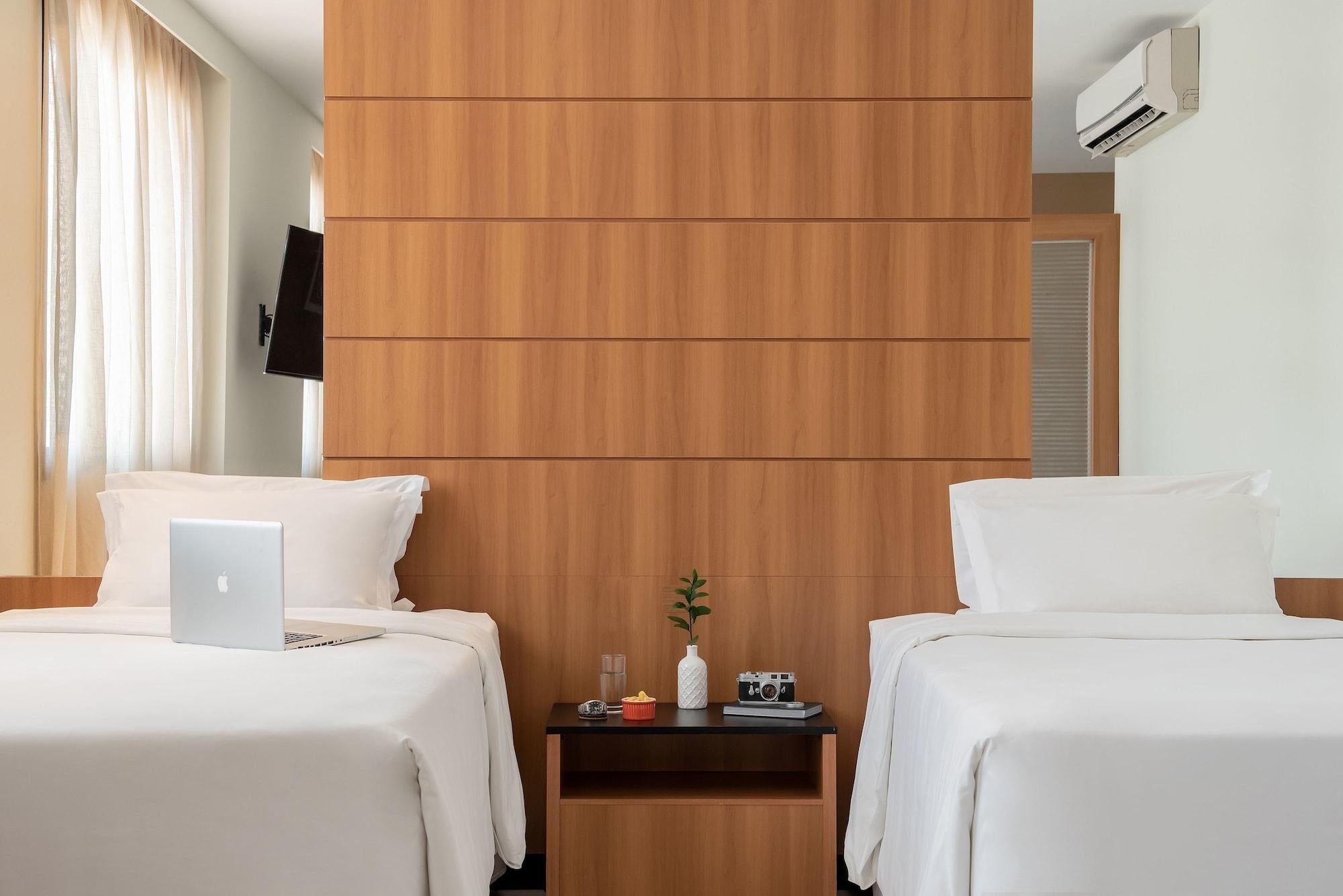 Habitación de hotel con dos camas, cabecero de madera, televisión de pantalla plana y unidad de aire acondicionado.