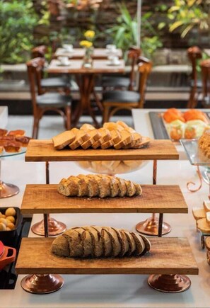 Ein Essbereich mit Holztischen und -stühlen, einer Auswahl an Brot auf Präsentationsständer und einem Garten im Hintergrund.