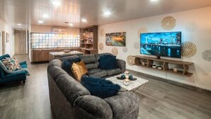 Een moderne woonkamer met een grijze hoekbank, een salontafel en een flatscreen televisie aan de muur.