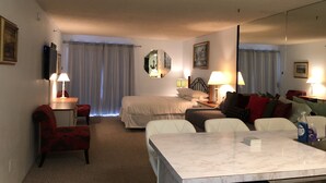 Quarto de hotel com cama, secretária com cadeira, mesa de jantar e sofá.
