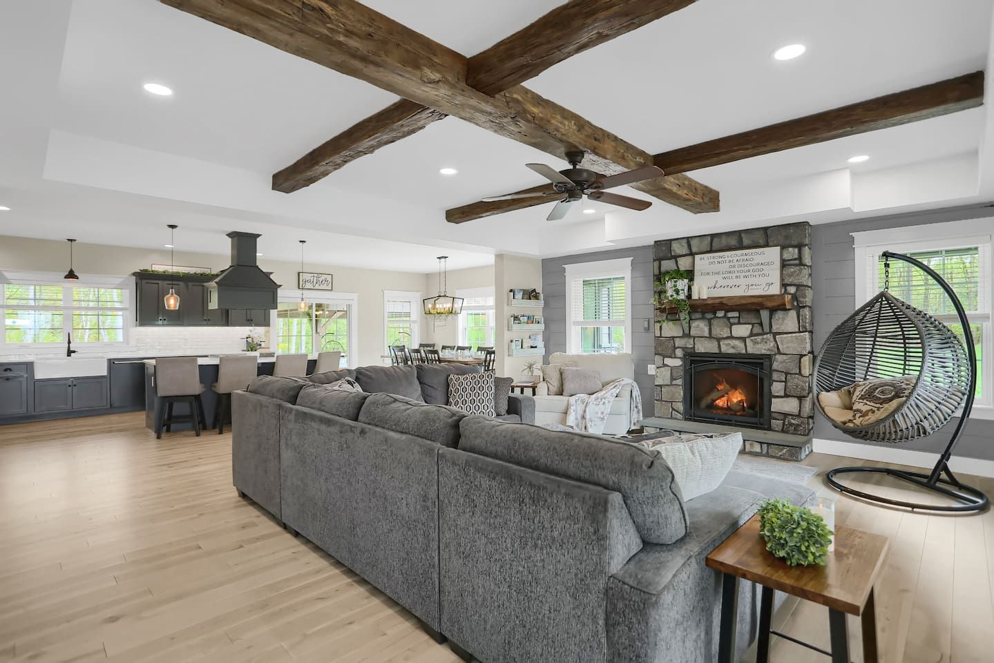 A spacious living area with a large gray sectional sofa, a stone fireplace, and a hanging chair.