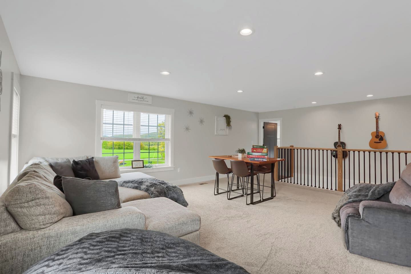 A spacious living room with a large window, a dining area, and a balcony with two guitars.