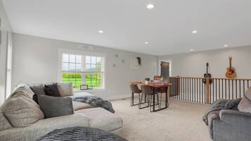A spacious living room with a large window, a dining area, and a balcony with two guitars.