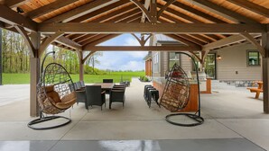 Eine überdachte Terrasse mit Sitzgelegenheit, darunter Stühle und ein Tisch, sowie ein Grill.