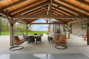 Eine überdachte Terrasse mit Sitzgelegenheit, darunter Stühle und ein Tisch, sowie ein Grill.