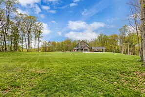 Een groot, open veld met een laaggelegen huis met een stenen schoorsteen, omringd door bomen.