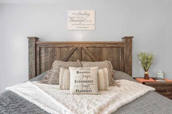 Una cama bien hecha con un cojín decorativo y una cita motivacional en la pared superior.