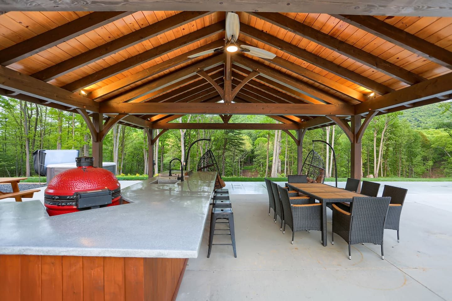 Eine überdachte Terrasse im Freien mit Grill, Esstisch und Stühlen.