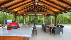 Eine überdachte Terrasse im Freien mit Grill, Esstisch und Stühlen.