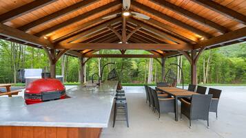 Eine überdachte Terrasse im Freien mit Grill, Esstisch und Stühlen.