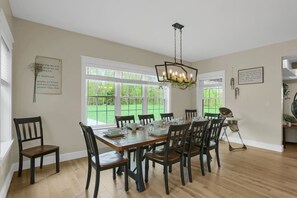 Comedor con mesa de madera dispuesta para seis comensales, sillas, ventanas amplias y una lámpara de araña.