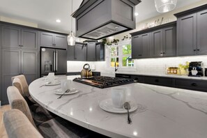 A modern kitchen with a curved island, grey cabinetry, and a stainless steel refrigerator.
