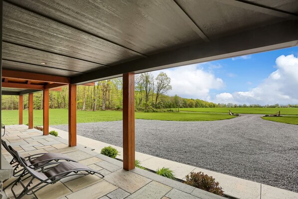 A covered outdoor seating area with a gravel driveway leading to a green field.