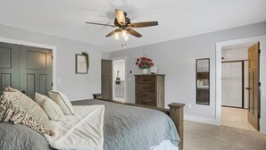 Ein Schlafzimmer mit einem Bett, einem Deckenventilator, einer Kommode und einer Tür zu einem anderen Raum.