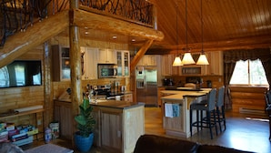A rustic cabin interior with a kitchen, dining area, and a loft bedroom. - Waterfront Log Home | Private Dock | Expansive Beautiful Yard and Gardens (Sagle)