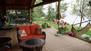 A wooden deck with outdoor furniture, including a sofa and chairs, and a hanging chair. - Waterfront Log Home | Private Dock | Expansive Beautiful Yard and Gardens (Sagle)
