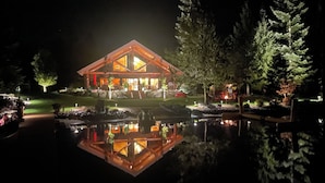 A lodge with a large wooden structure, a reflection pool, and surrounding trees. - Waterfront Log Home | Private Dock | Expansive Beautiful Yard and Gardens (Sagle)