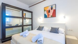 Una habitación de hotel con una cama, un espejo grande, un cuadro y una mesita de noche.