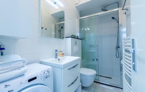 Une salle de bain moderne avec une douche à parois de verre, un lavabo blanc et un porte-serviettes à plusieurs niveaux.