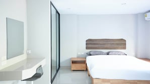 A modern bedroom with a large bed, a bedside table, a mirror, and a sliding glass door. - Baan Pakdi (Pattaya)