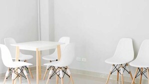 A modern, minimalist room with a white table and chairs, a white air conditioning unit on the wall, and a plain white wall. - Baan Pakdi (Pattaya)
