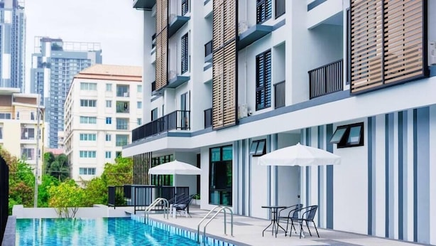 A modern apartment building with a swimming pool, outdoor seating, and a view of surrounding high-rise buildings. - Baan Pakdi (Pattaya)