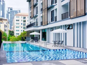 A modern apartment building with a swimming pool, outdoor seating, and a view of surrounding high-rise buildings. - Baan Pakdi (Pattaya)