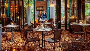 An indoor dining area with tables set for two, surrounded by wicker chairs, and a view of the street through large windows. - Balthazar Design Hotel (Kraków)