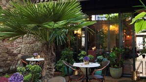 An outdoor patio area with brick flooring, wicker chairs, a table with a vase of flowers, and potted plants. - Balthazar Design Hotel (Kraków)
