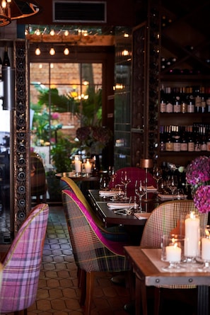 Ein Restaurantinnenraum mit einem für zwei Personen gedeckten Tisch, umgeben von Stühlen, und einem Weinkühlschrank im Hintergrund.