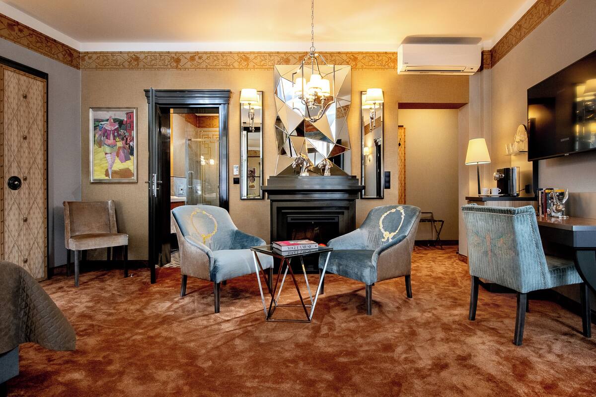 A hotel room with a fireplace, two armchairs, a coffee table, and a TV.