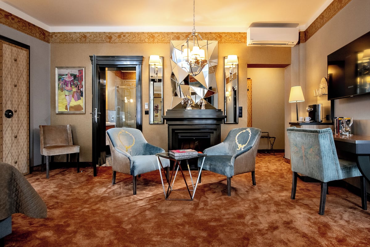 A hotel room with a fireplace, two armchairs, a coffee table, and a TV.
