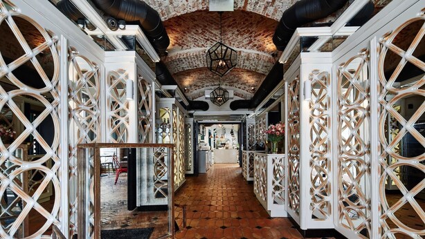 A corridor with ornate white lattice partitions, a brick ceiling, and a tiled floor. - Balthazar Design Hotel (Kraków)
