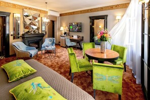 A hotel room with a fireplace, a dining area, and a seating area with green upholstered chairs and a sofa. - Balthazar Design Hotel (Kraków)