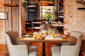A restaurant with a brick wall, a wine rack, and a table set for two with plates of food and drinks. - Balthazar Design Hotel (Kraków)
