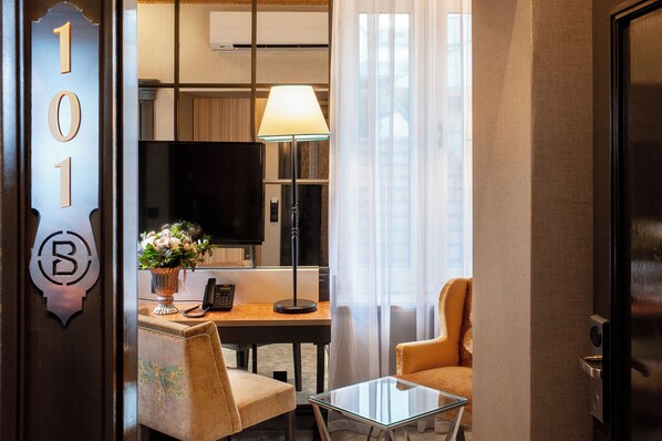 A hotel room with a desk, a chair, a glass table, a lamp, a TV, and a floral arrangement. - Balthazar Design Hotel (Kraków)