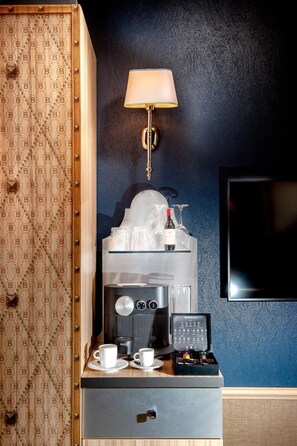 A minibar with a coffee machine, two cups, a wine bottle, and a TV mounted on a dark wall. - Balthazar Design Hotel (Kraków)