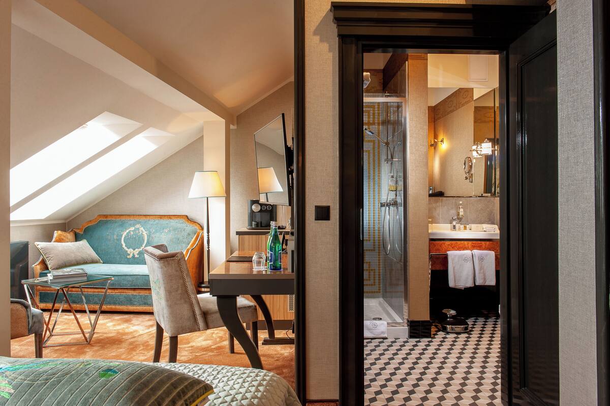 A hotel room with a loft bed, a sofa, a desk, and a bathroom with a shower and sink.