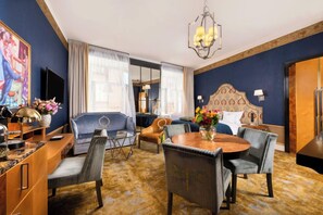A hotel room with a large bed, a sitting area with a sofa and chairs, a dining table with chairs, a TV, and a large painting on the wall. - Balthazar Design Hotel (Kraków)