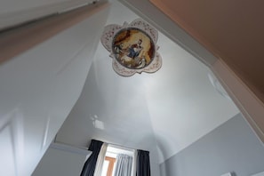Ein Zimmer mit hoher Decke, einer dekorativen Deckenmedaillon, einem mit Vorhängen versehenen Fenster und einer Tür.