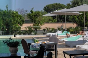 Un área junto a la piscina con mesa lista para comer, sillas de descanso y sombrillas.