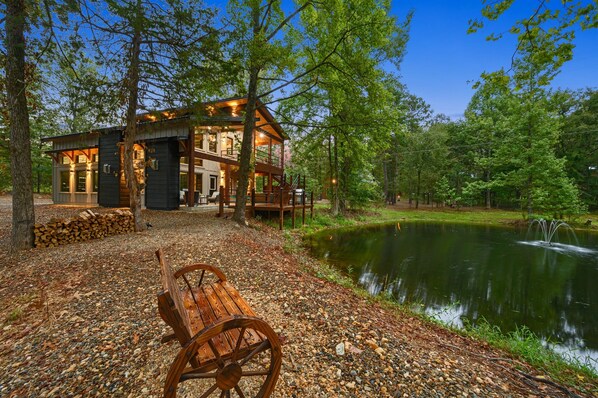 A cabin with a deck, a pond, and a wooden bench.